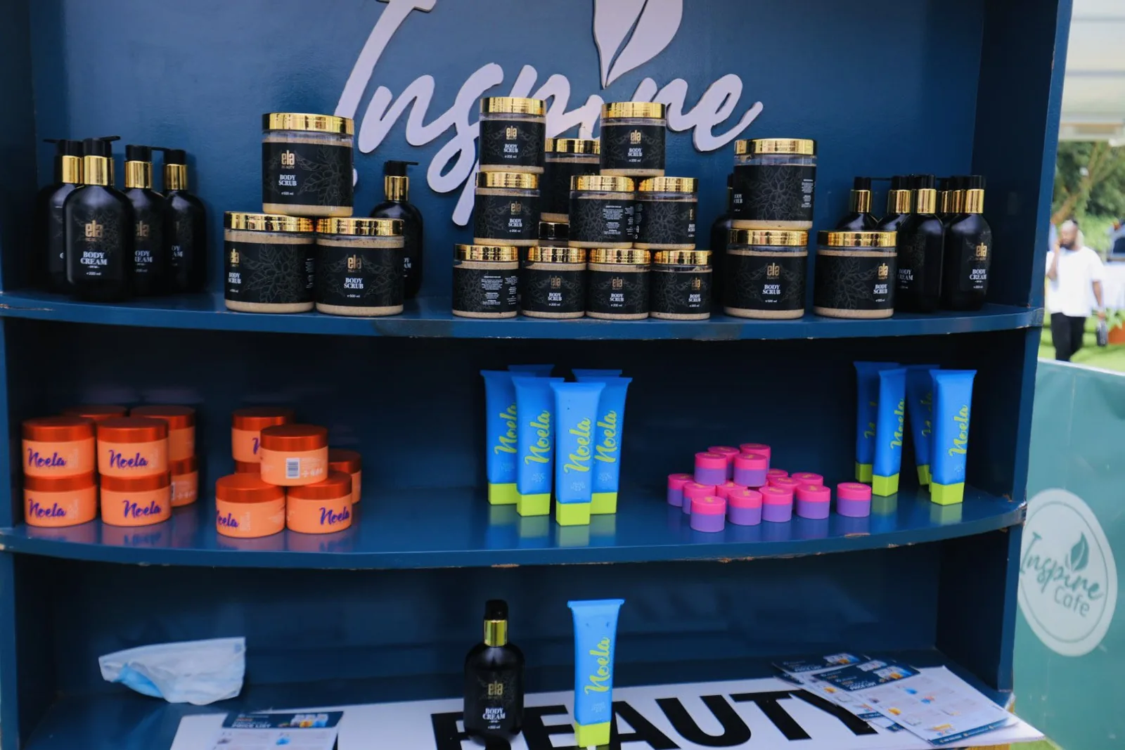 The Inspire skincare stand: Ela Beauty body cream and scrub in black and gold on the top shelf, the orange, blue and pink Neela range below