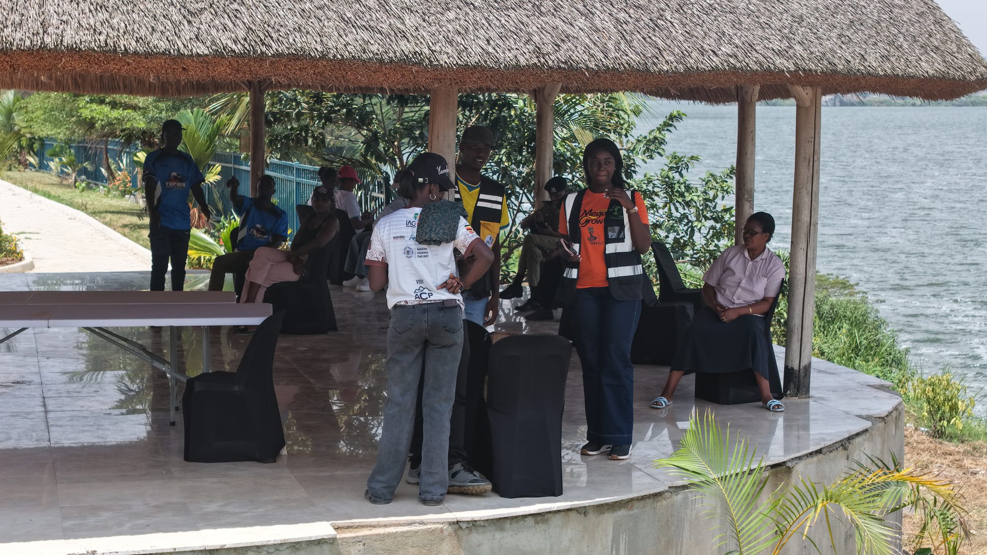 Guests under a thatched pavilion on the Nyabihoko shoreline with the lake behind