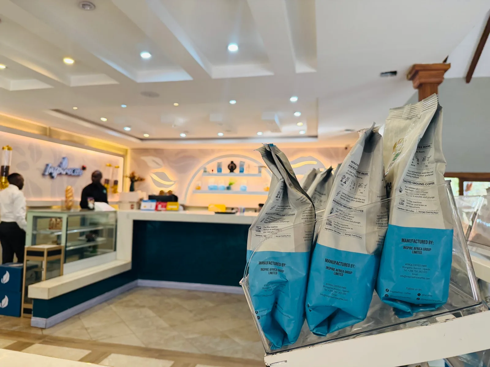 Blue-and-white bags of Inspire coffee in the foreground at Inspire Café, with the café counter and a member of staff in the background.