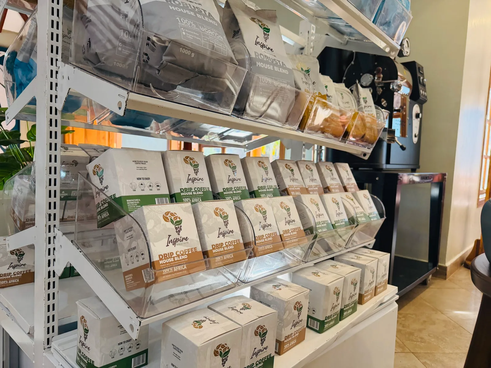 Rows of Inspire Drip Coffee House Blend boxes on a slanted display rack, with more bagged coffee on the shelf above.
