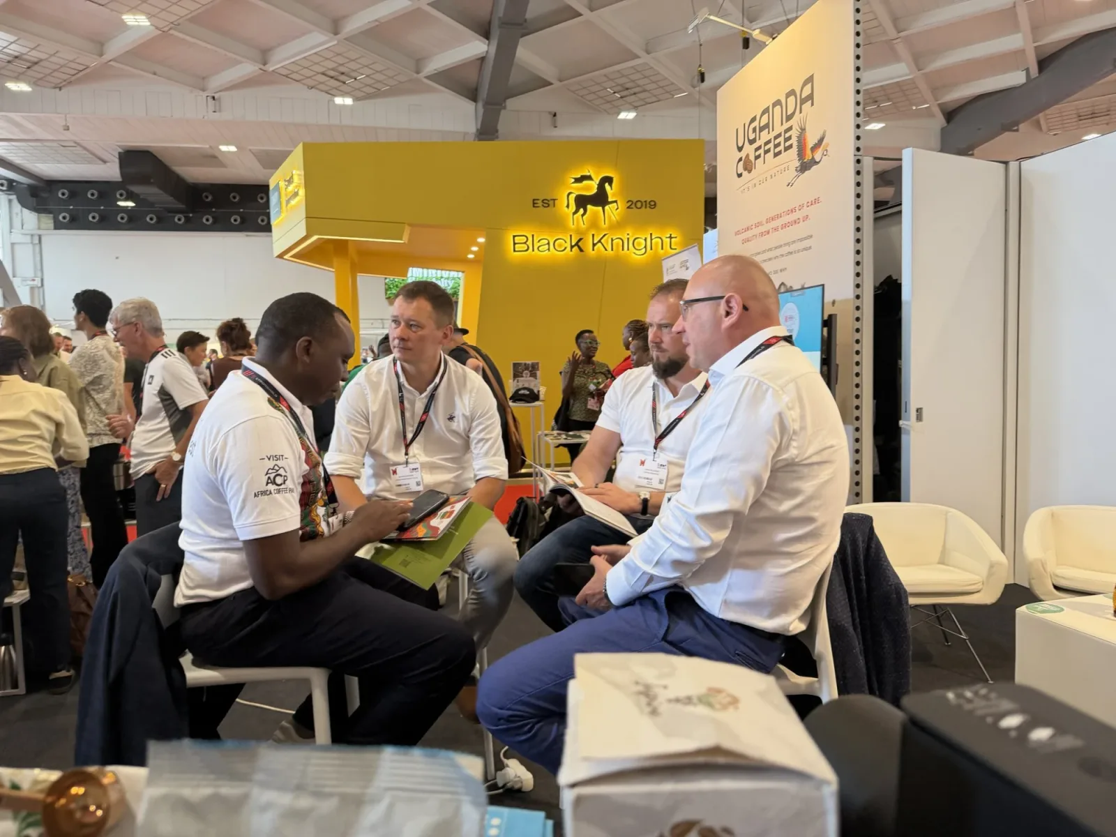 An Africa Coffee Park delegate in a Visit ACP shirt meeting European buyers at the Uganda Coffee stand, World of Coffee Brussels.