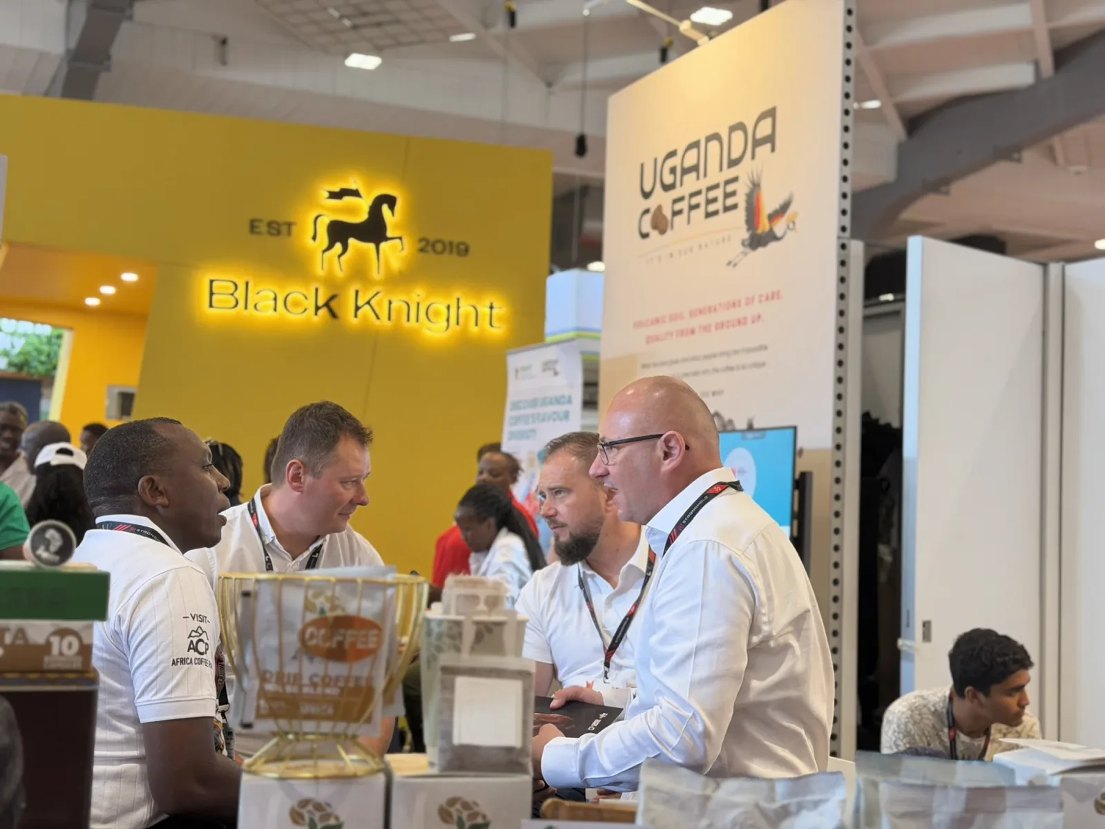 An Africa Coffee Park delegate talking with European buyers beside a display of coffee packs